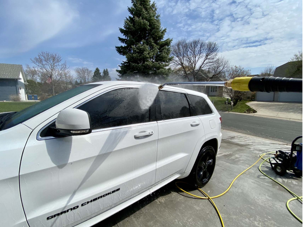 A car being washed with a jet wash, focusing on the water spray hitting the side windows and door.