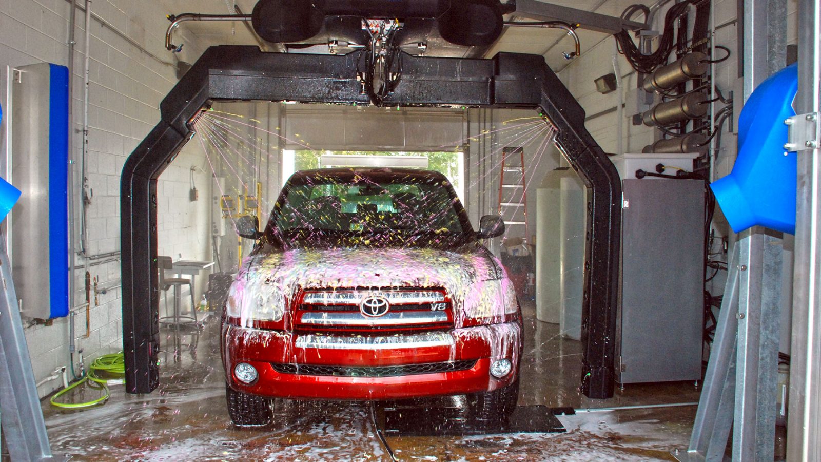 A red car going through an automatic car wash with a soap