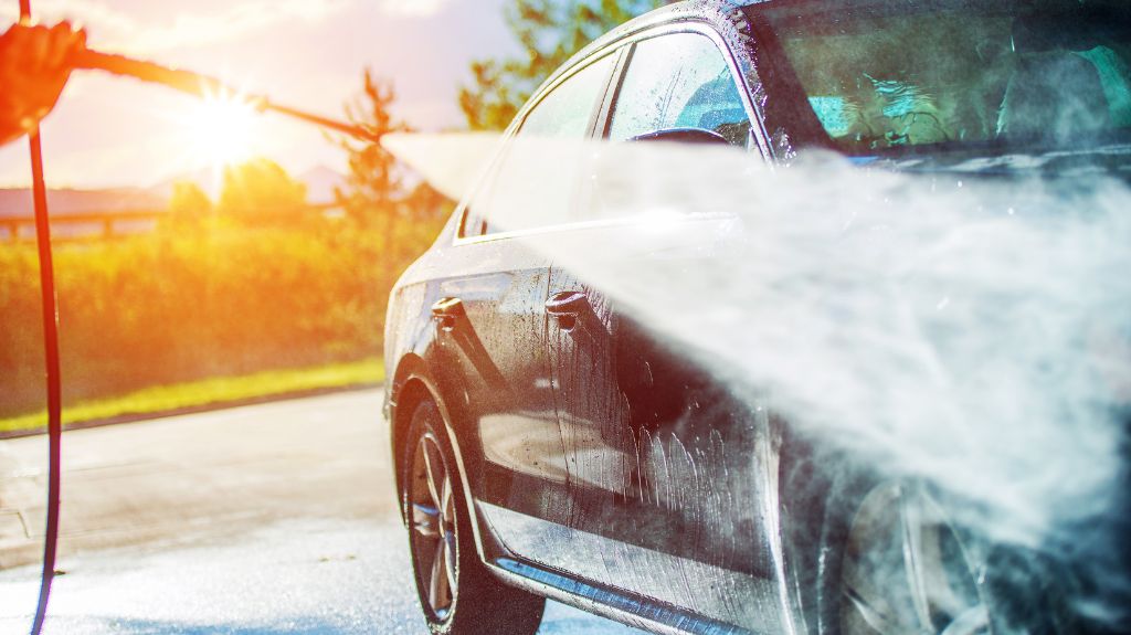 A person using a high-pressure hose to wash a car, illustrating the difference between car detailing and car wash.