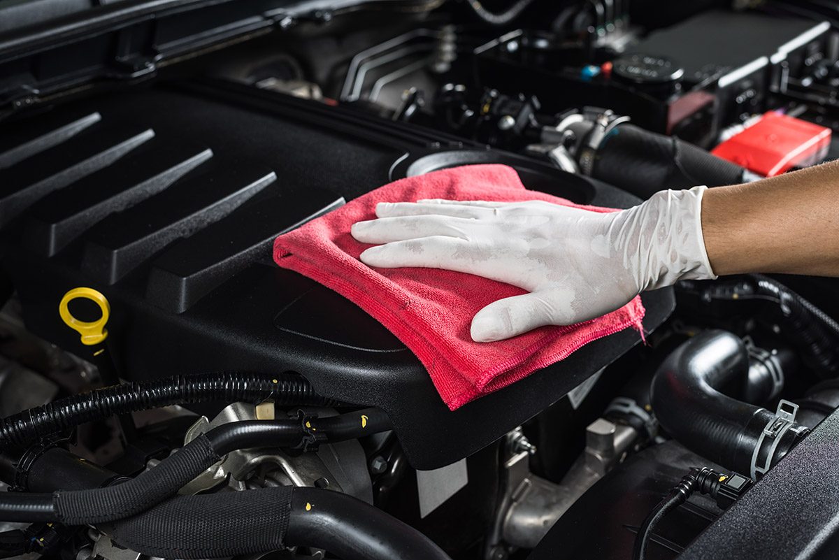 Professional car valet service cleaning engine with a red microfiber cloth and gloves