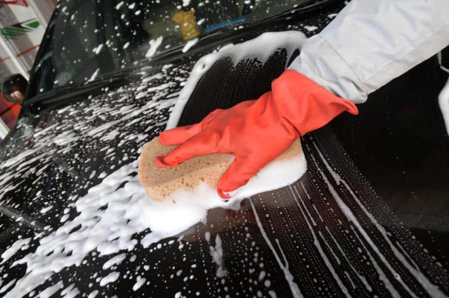 Person washing a car with soap and sponge, wearing red gloves