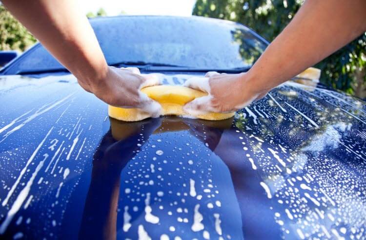 Hands washing a car with a sponge and soapy water