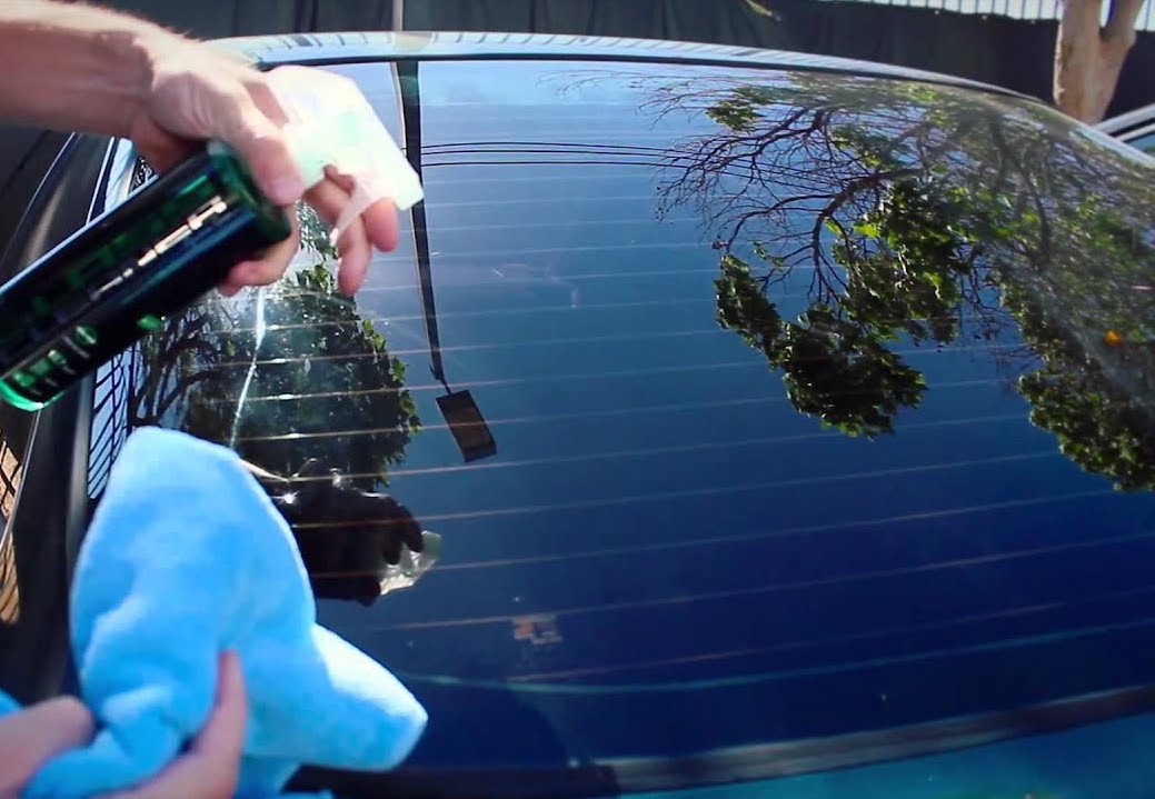 Hand using a spray bottle and cloth to clean a car's rear window