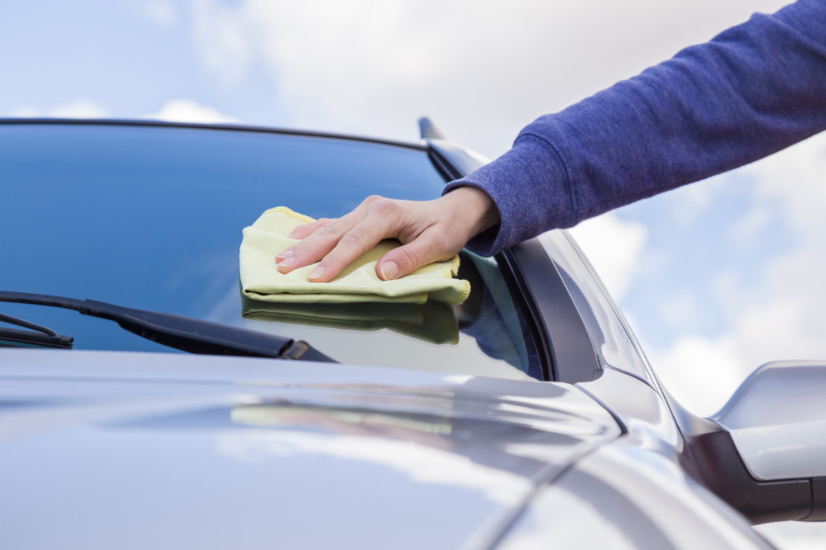 Hand cleaning a car windshield with a yellow cloth, ensuring a streak-free finish.