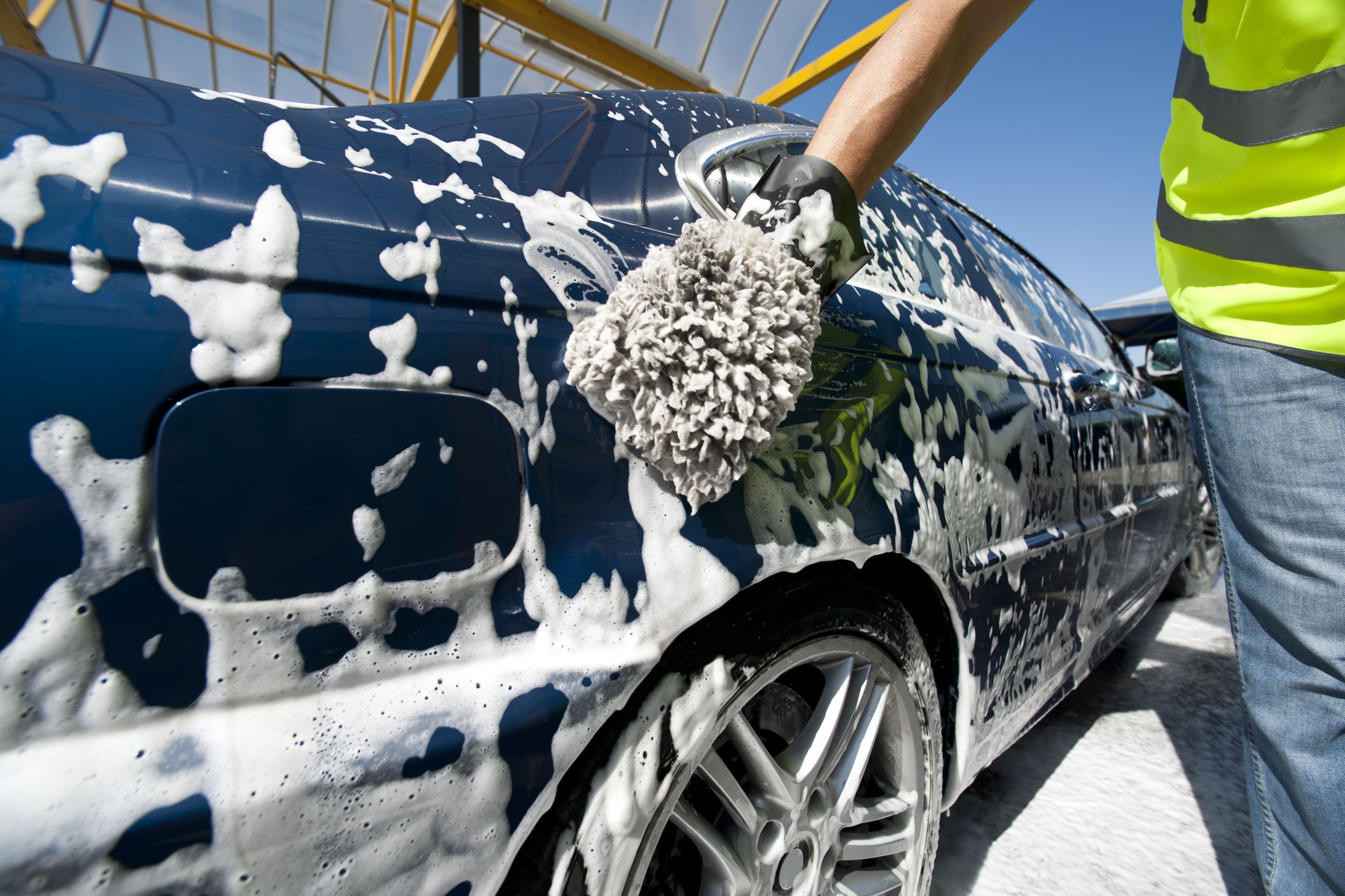 Car being hand washed with a foam mitt, covered in soap suds