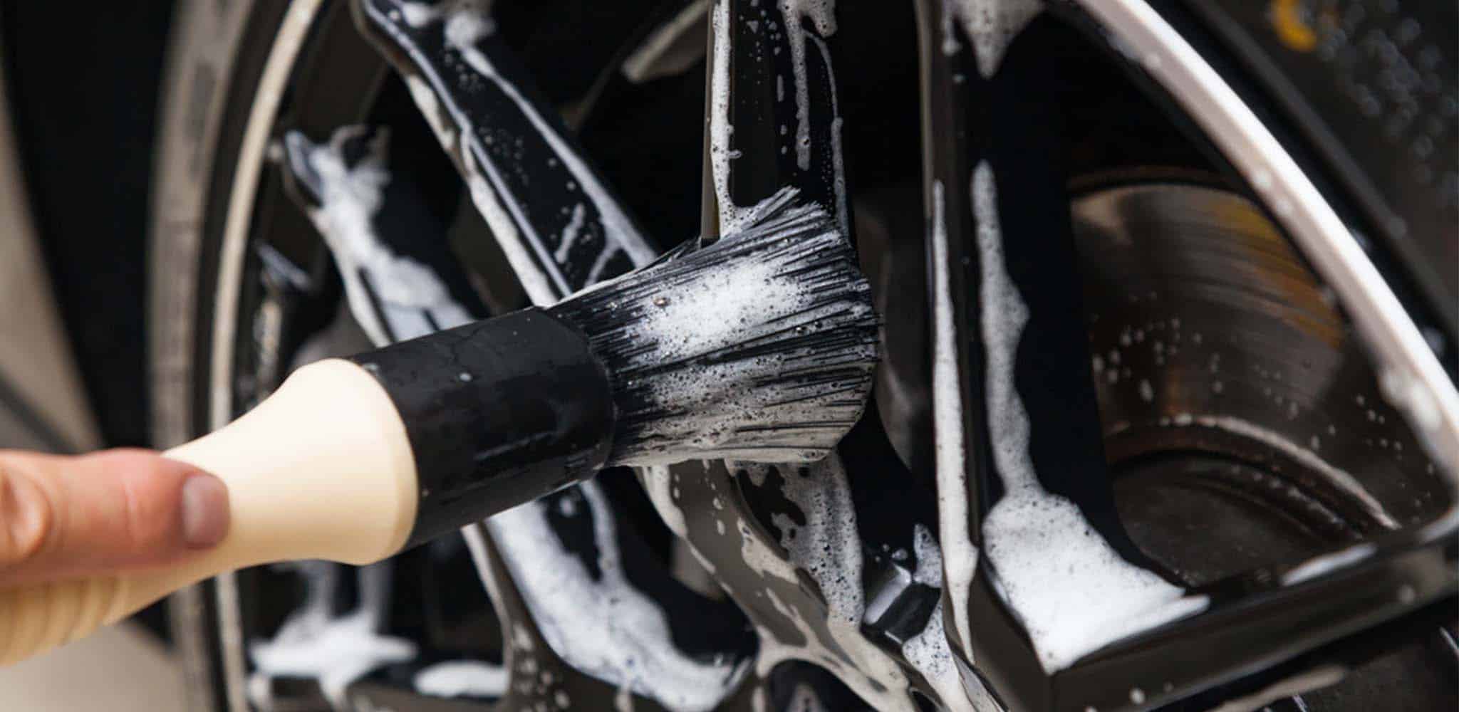 Close-up of a brush cleaning an alloy wheel with soap