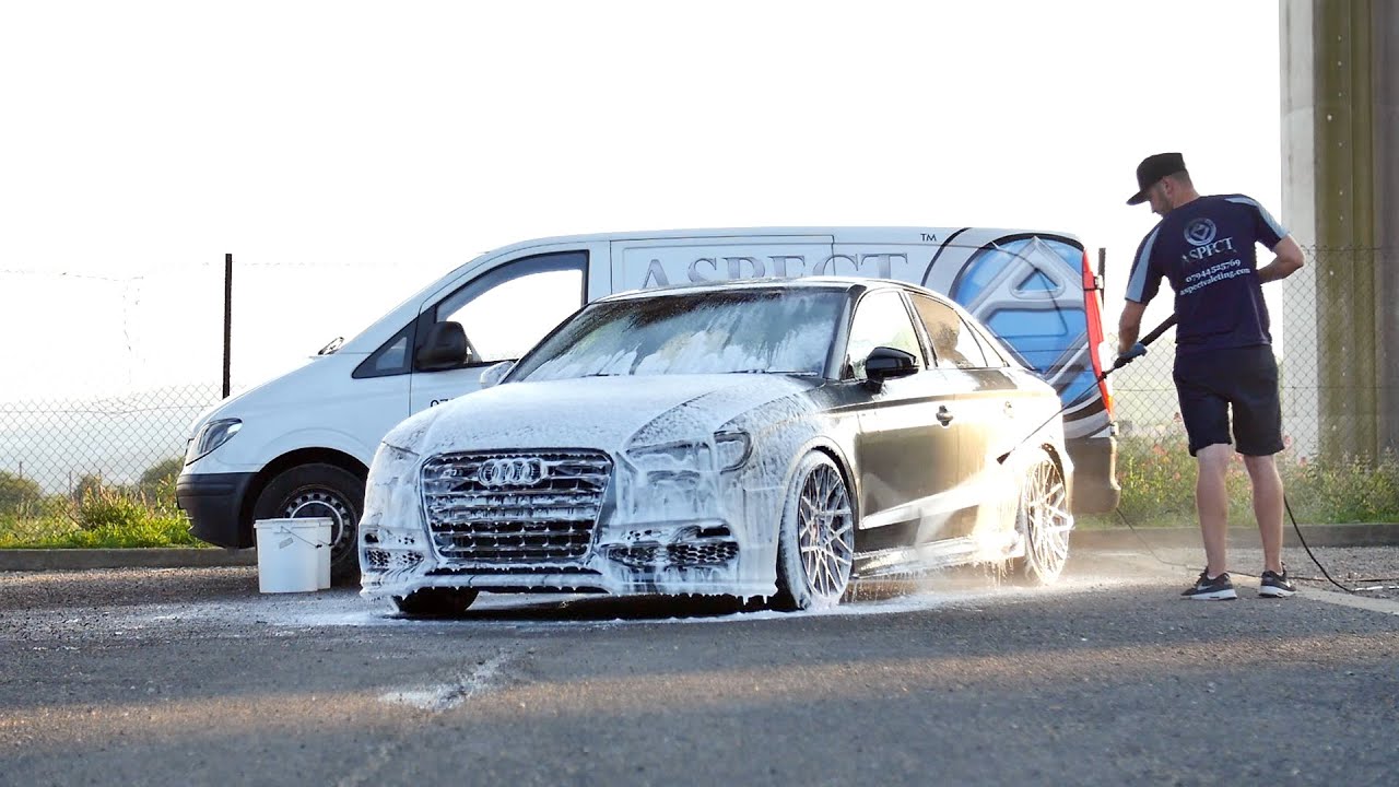 A professional mobile detailer washing a car with a high-pressure hose and foam, demonstrating the convenience of mobile detailing services.