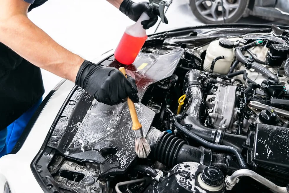 Professional cleaning and detailing of a car engine bay with a detailing brush and cleaning spray bottle.