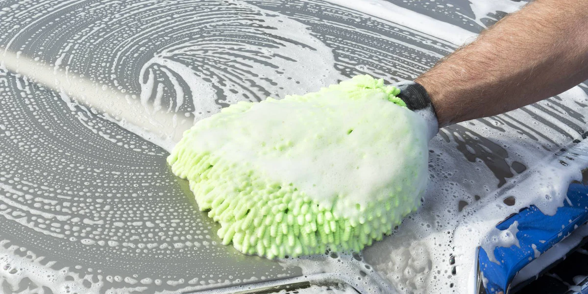 Hand washing a car with a green microfibre mitt and foamy soap on a car hood