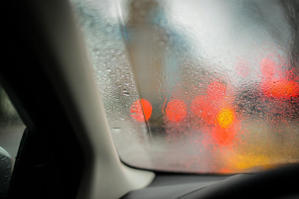 Fogged-up car window with blurred red and yellow lights visible outside