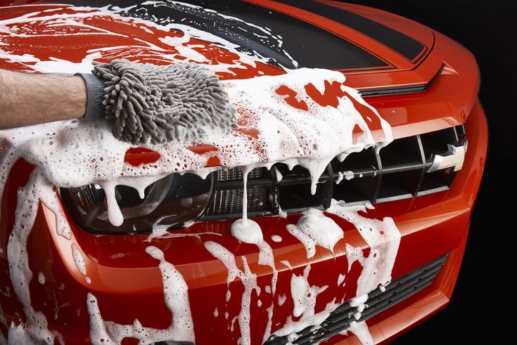 Hand using a soapy mitt to wash the front of a red car