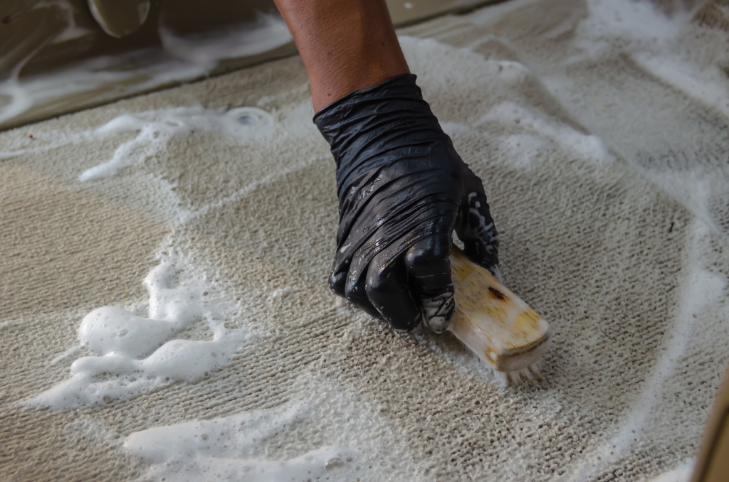 Person scrubbing a car carpet with a brush and soapy water, demonstrating thorough cleaning techniques.