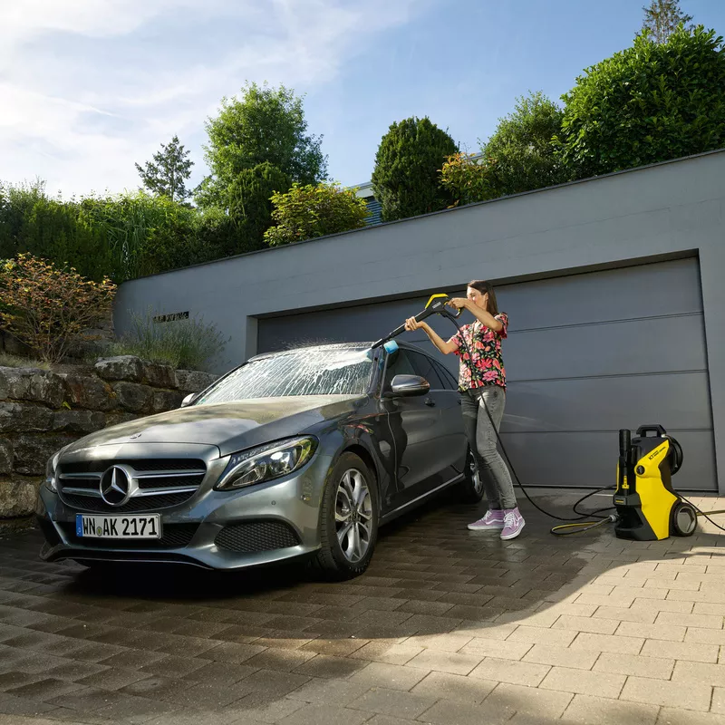 Person using a Karcher jet wash to clean a car in a driveway, demonstrating the effectiveness of different Karcher jet wash models.