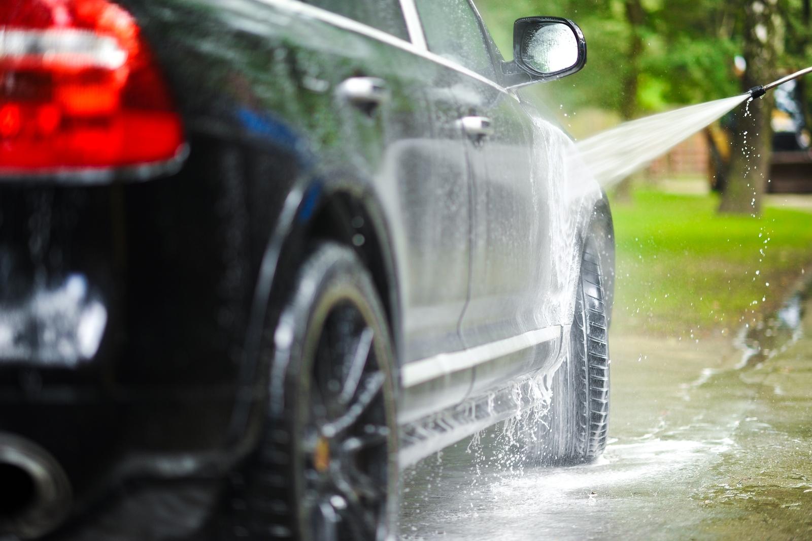 Pressure washing a black car with a high-pressure water hose