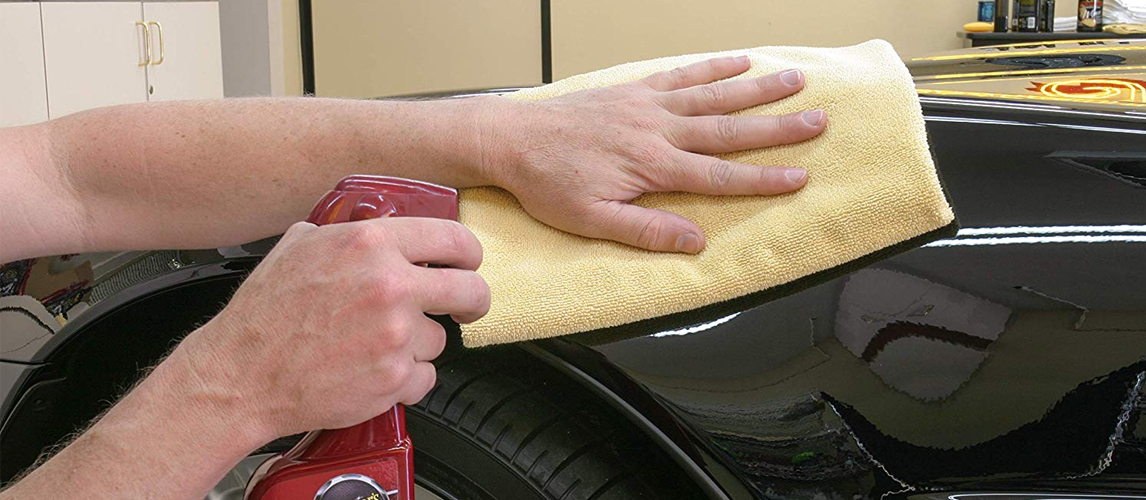 Hand using a yellow microfiber cloth and a spray bottle to clean a car surface