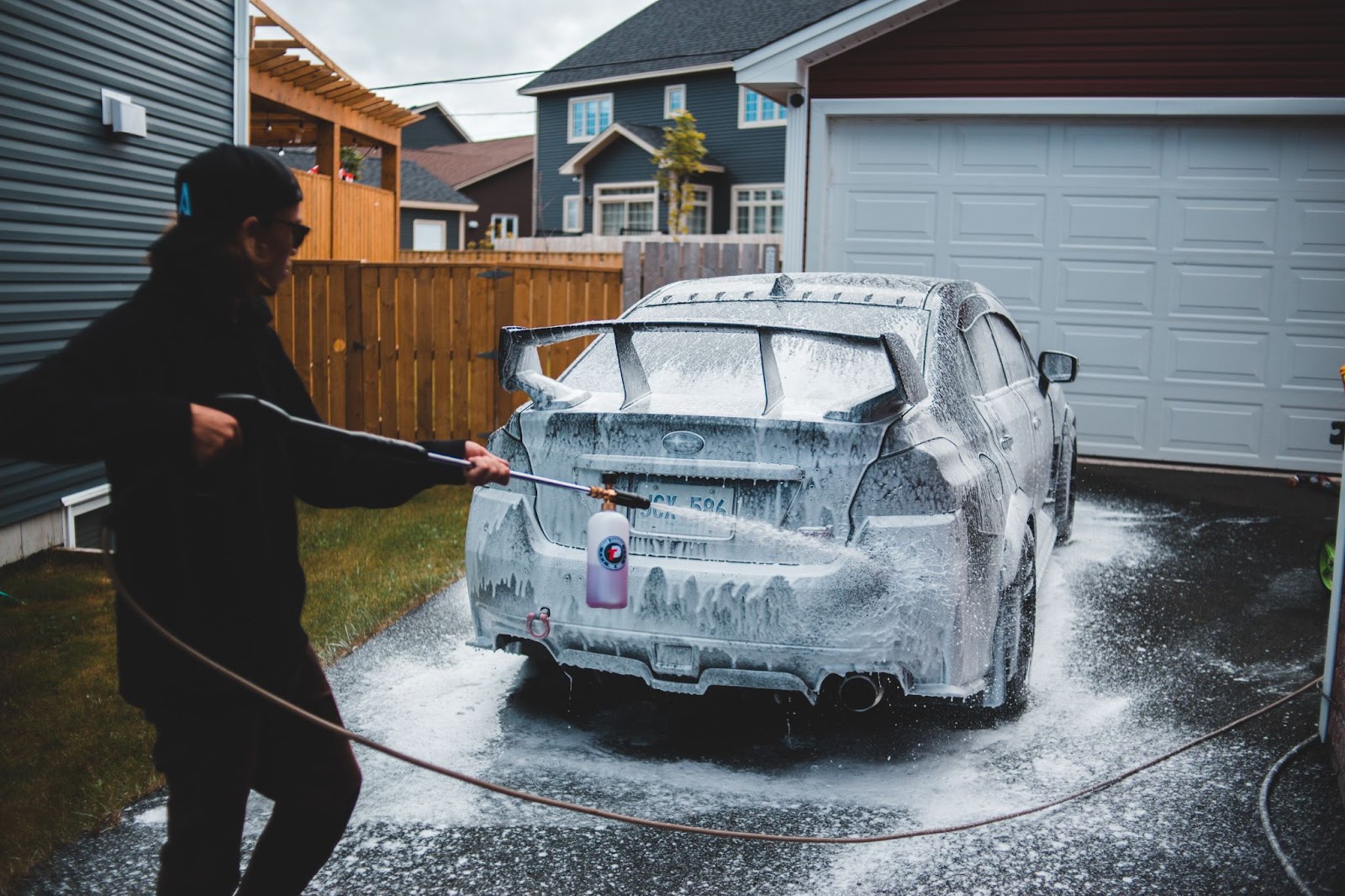 Person using a foam cannon to wash a car in a driveway