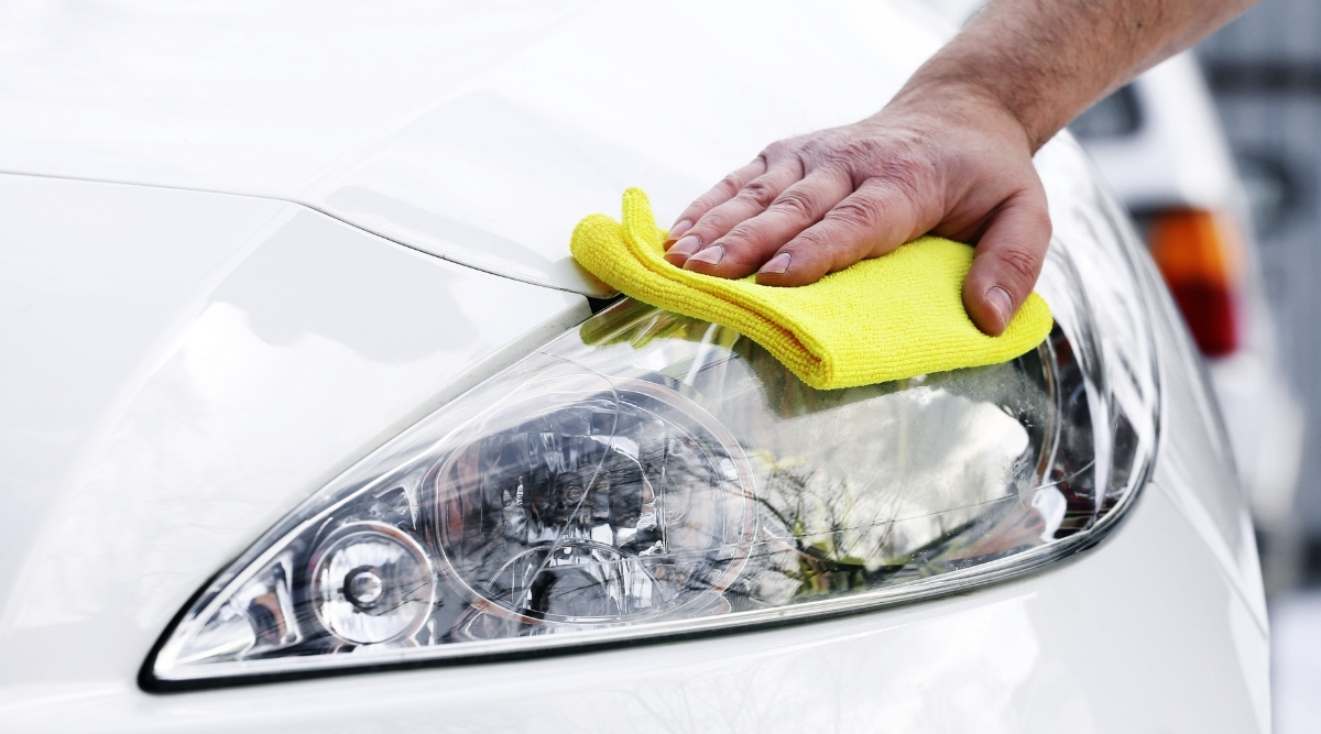 Hand wiping a car headlight with a yellow cloth during a waterless car cleaning session