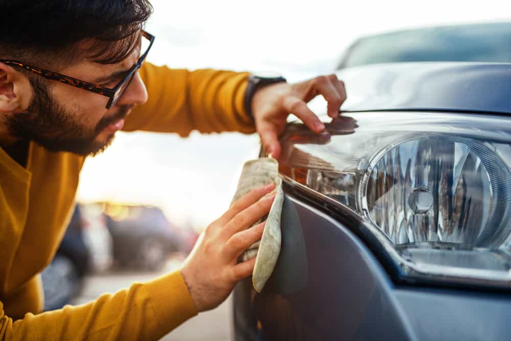 Professional detailer meticulously cleaning a car's headlight with a cloth, demonstrating the effectiveness of waterless wash and wax.