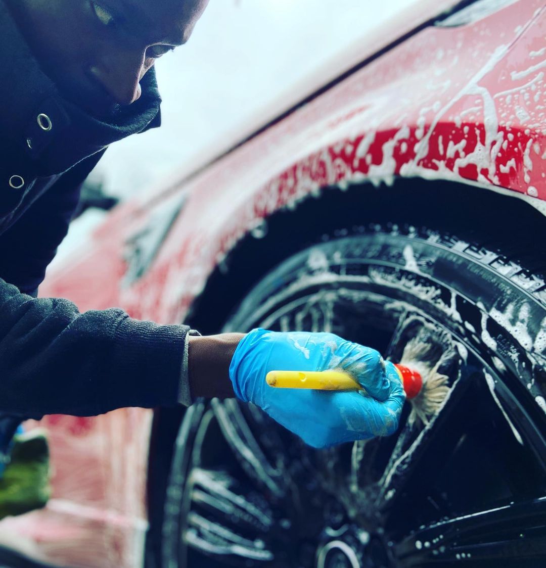 Professional car valet cleaning the wheels of a red car with a brush, demonstrating the detailed process of car valeting.