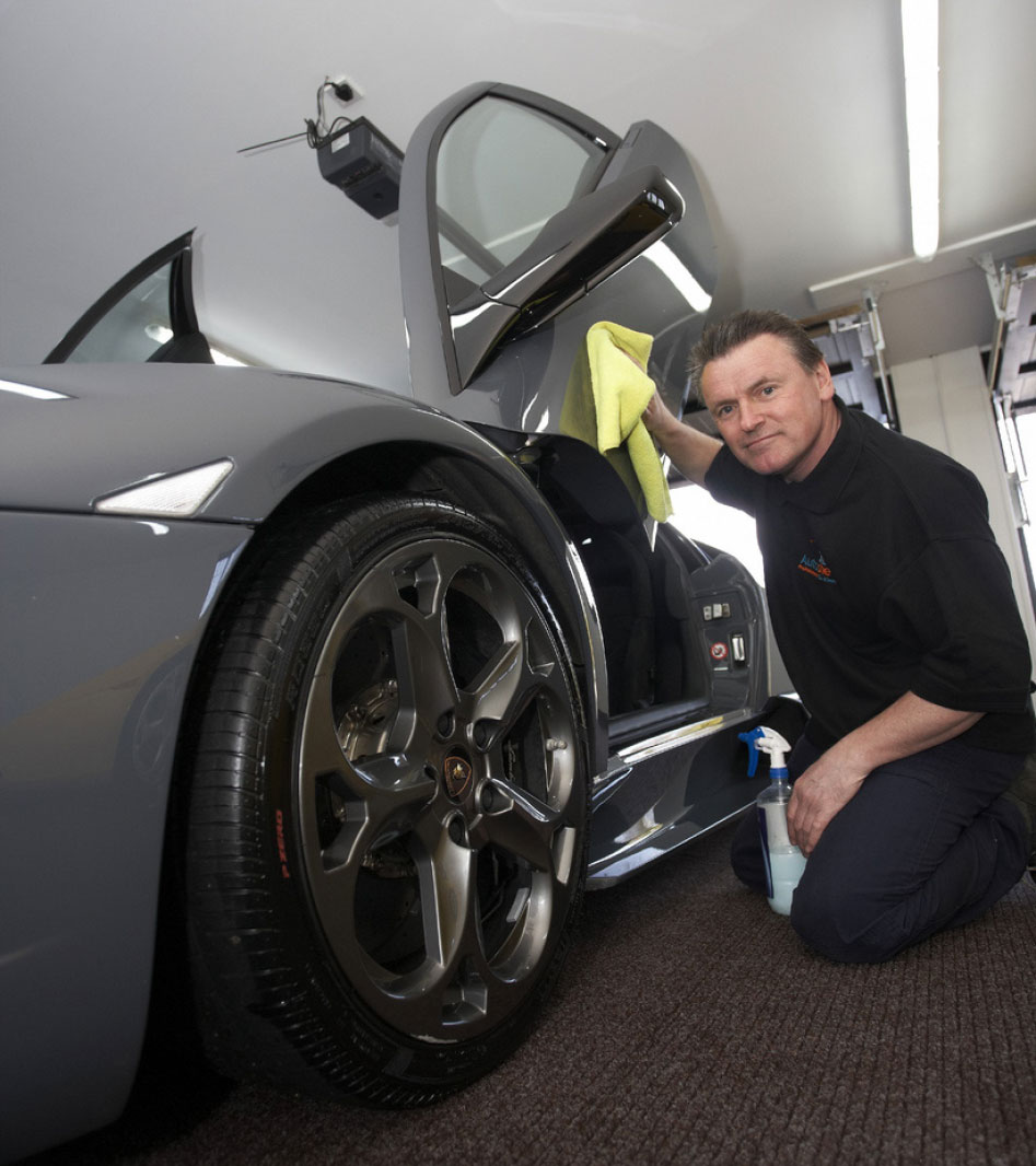 A professional car washer using a yellow cloth to clean a luxury car's door frame.