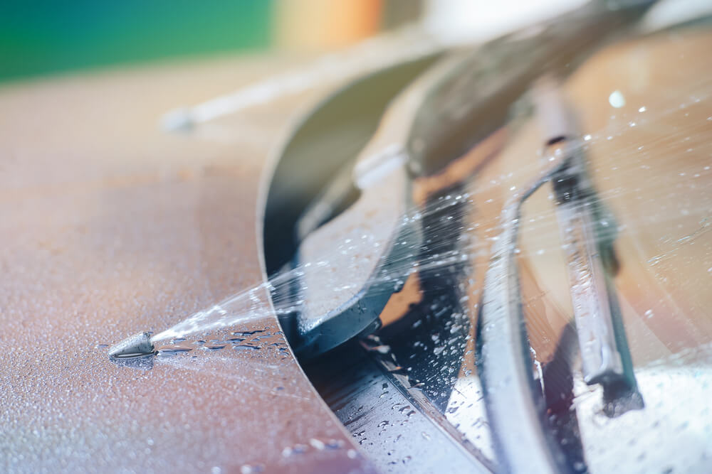 Close-up of a pressure washer hose spraying water on a car windshield