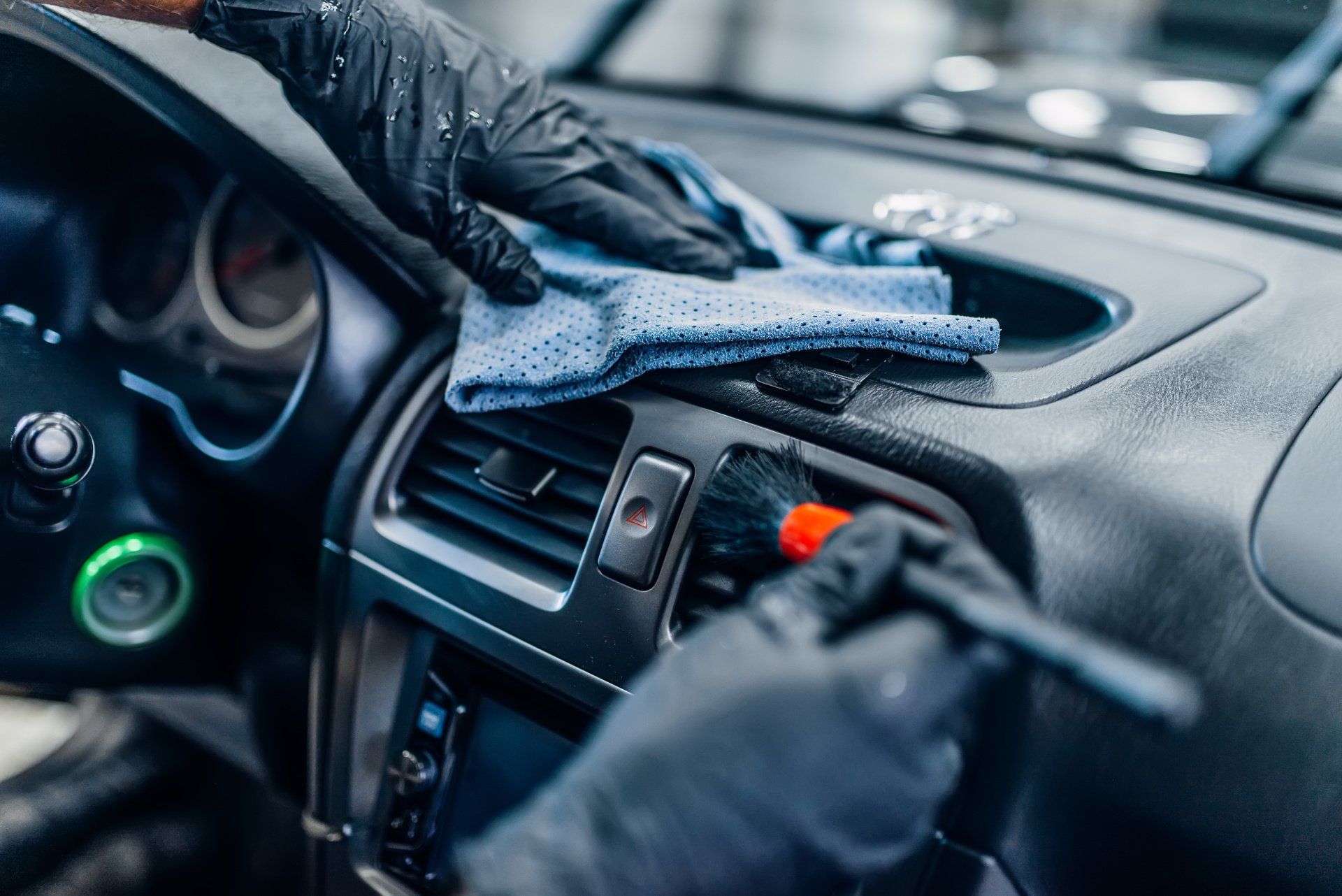 Close-up of hands in gloves cleaning a car interior with a cloth and brush.