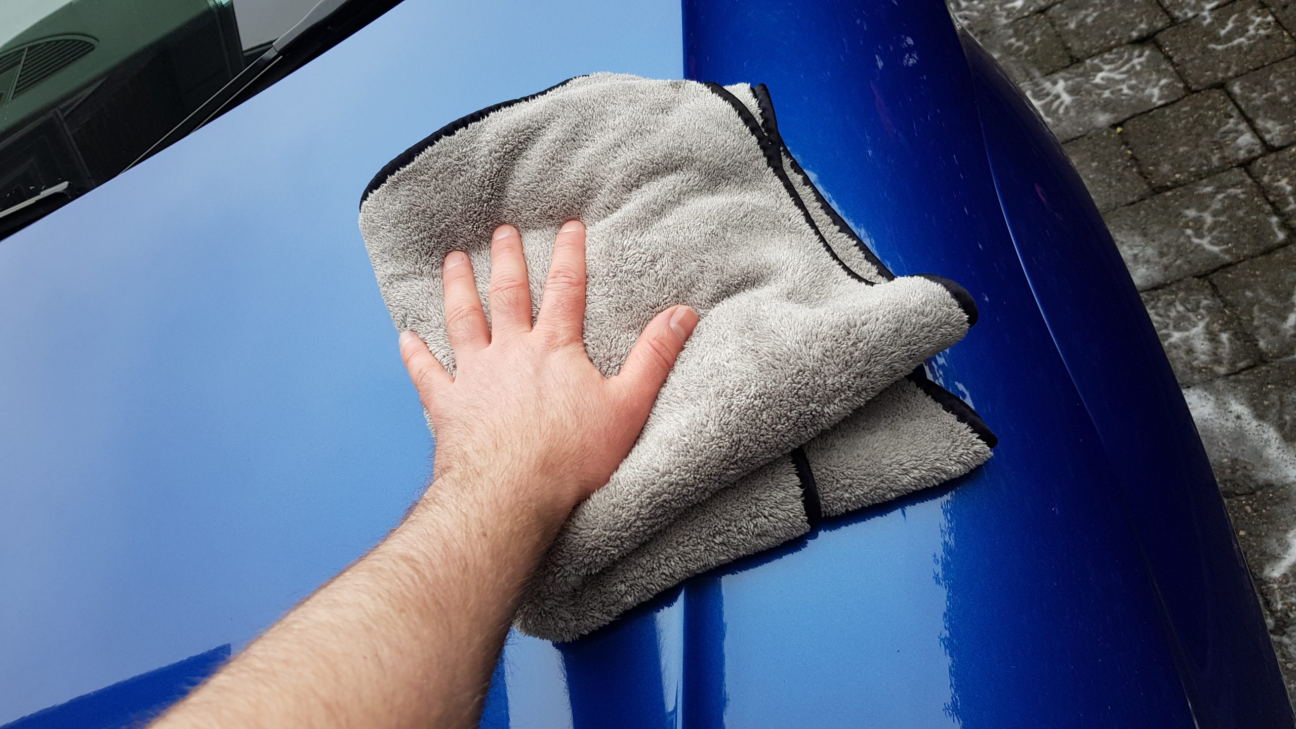 Hand applying car shampoo and wax on a blue car