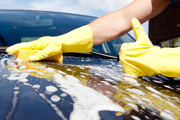 Person wearing yellow gloves using a sponge to wash a car with soap