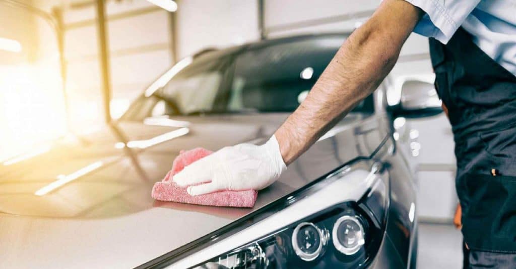 Professional car valeter polishing a car hood with a pink microfiber cloth.