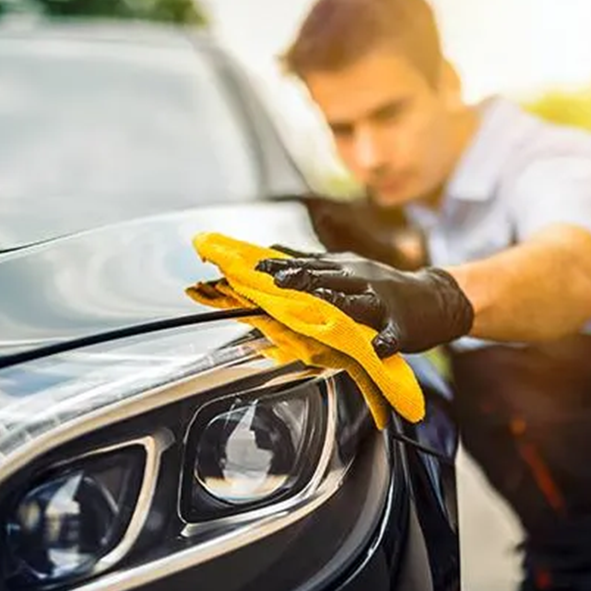 Professional car valet cleaning a car headlight with a yellow cloth.