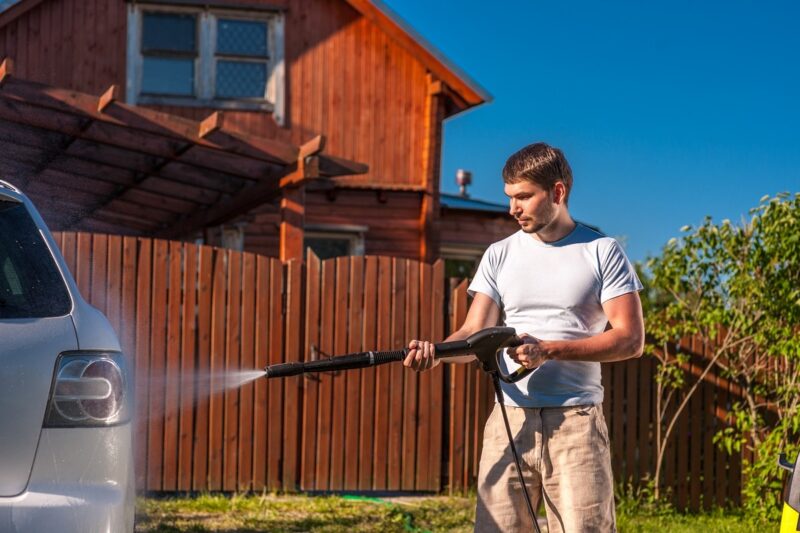 Man using a pressure washer to clean a car at home