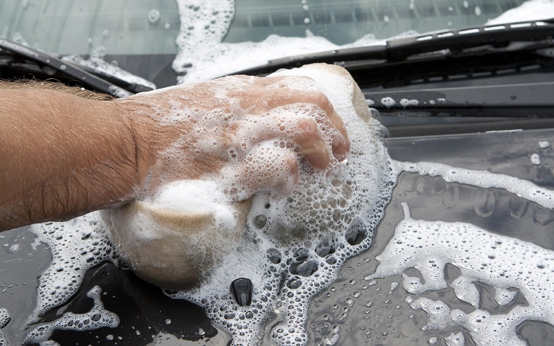 Hand using a sponge with car shampoo to wash a car