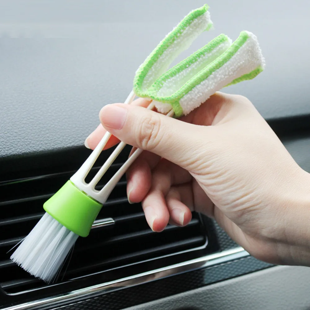 Close-up of a hand using a brush to clean car air vents, demonstrating car detailing tips.