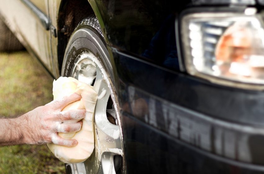 Close-up of a person washing a car wheel with a sponge using eco-friendly methods