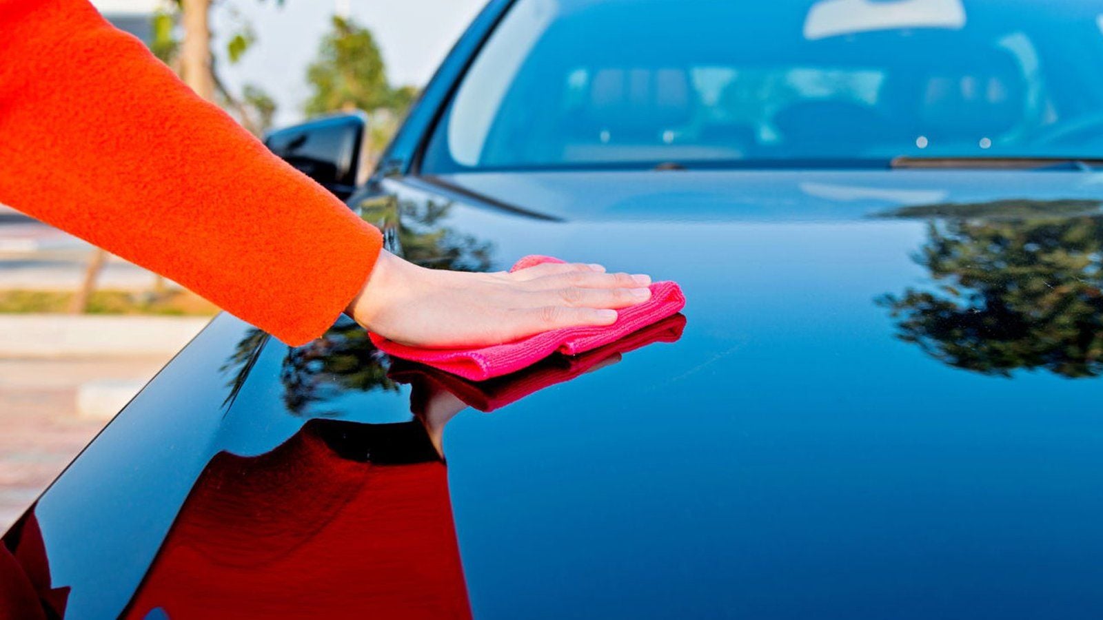 Hand wiping a black car with a red cloth at a hand wash car wash