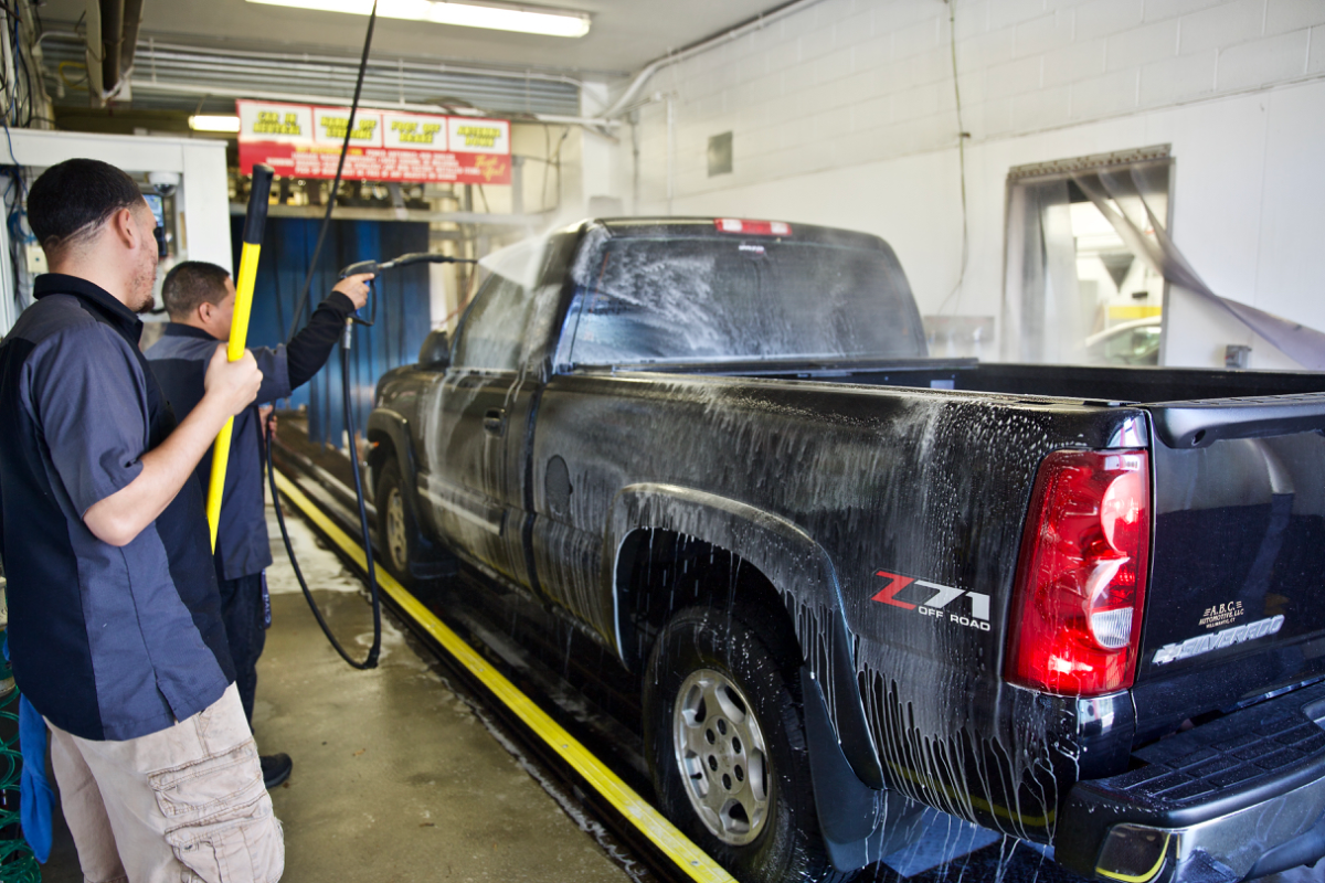 Professional car wash using a hot pressure washer to clean a black car.