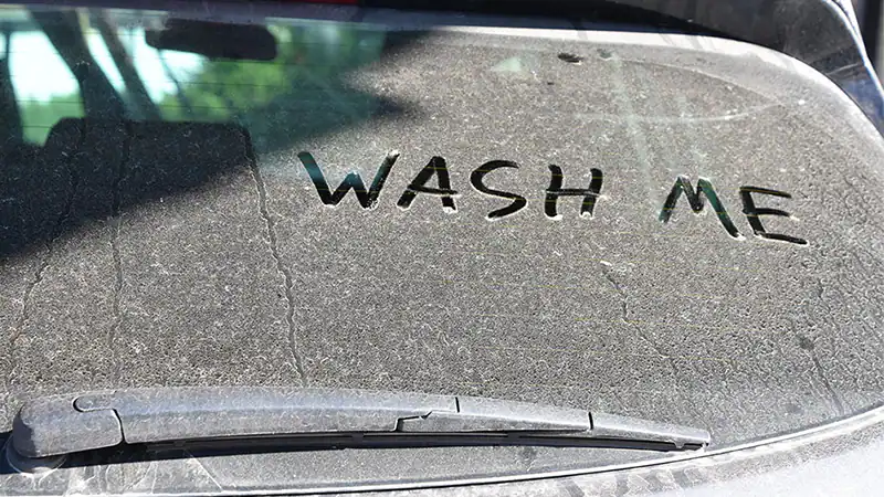 Dirty car rear window with "WASH ME" written in dust