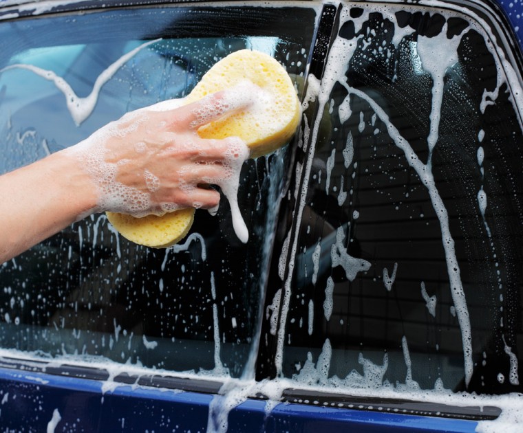 Close-up of a person using a sponge to wash a car window with soap and water