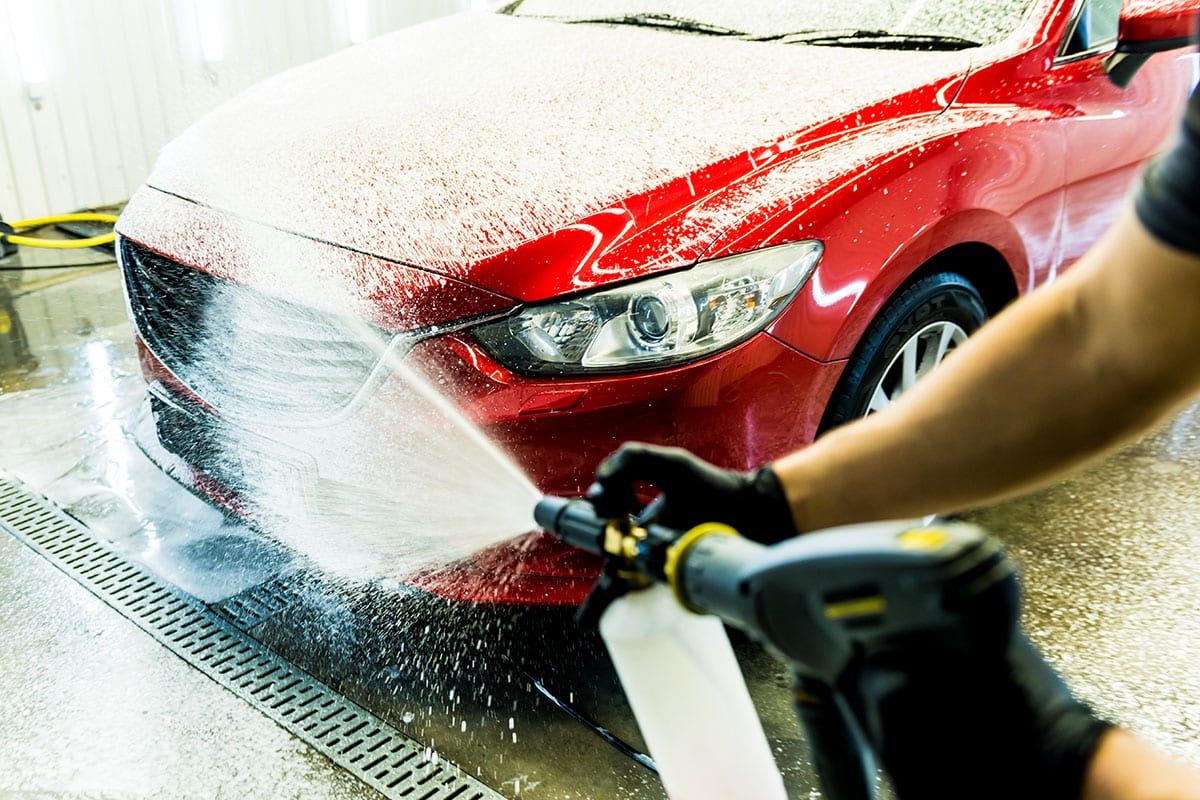 Red car being cleaned with a jet wash, highlighting the comparison between jet car wash and traditional car wash methods.