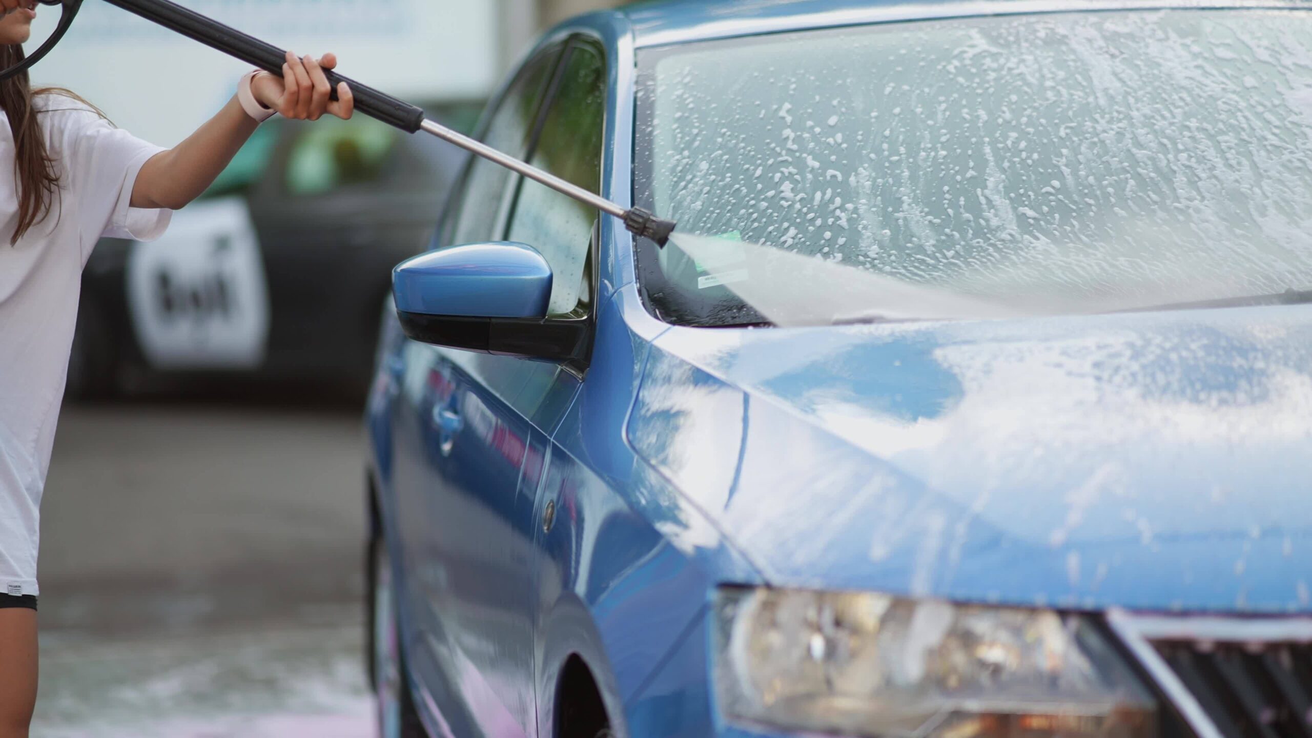 Woman using a jet wash to clean a blue car, demonstrating the effectiveness of DIY jet washing.