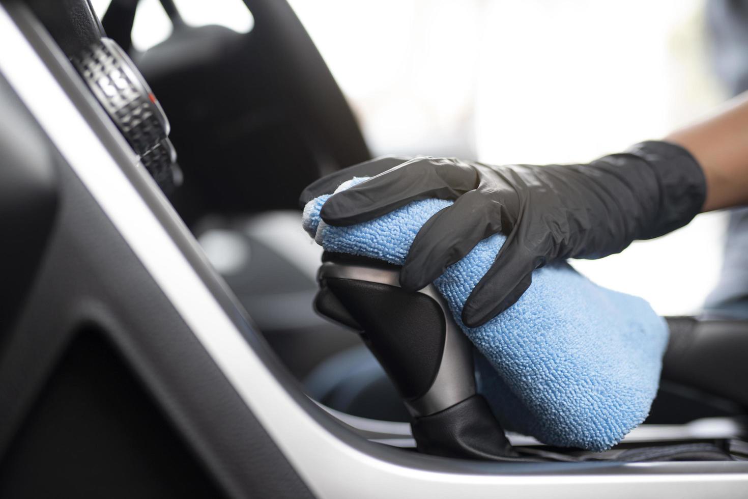 Close-up of a person wearing black gloves cleaning a car interior with a blue microfiber cloth.