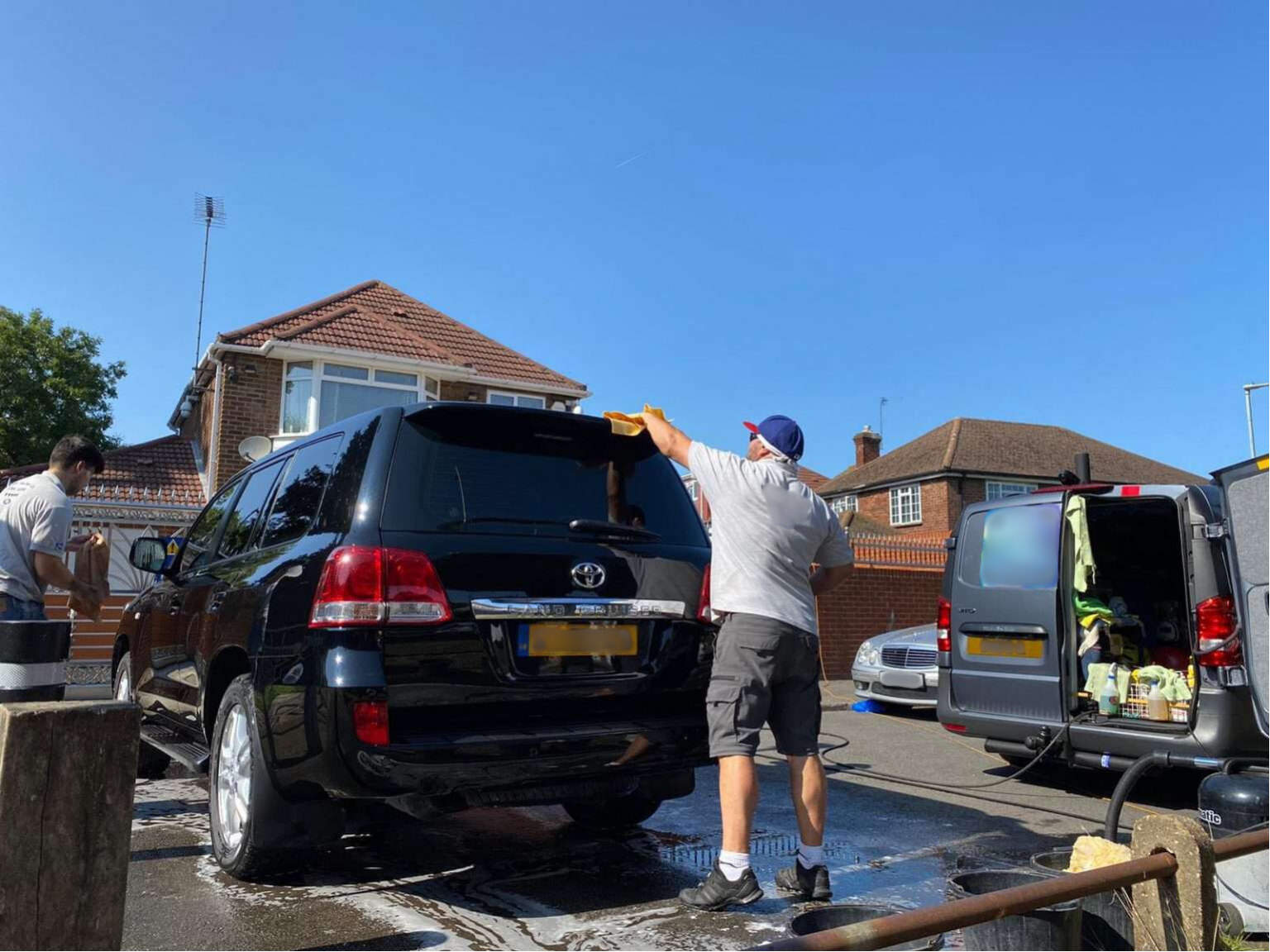 Two men performing mobile car valeting on a black car in front of a residential house