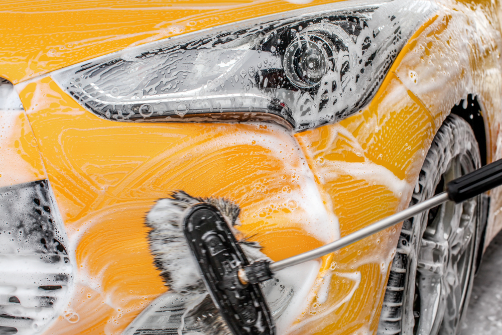 Close-up of a car being washed with a brush and soap suds