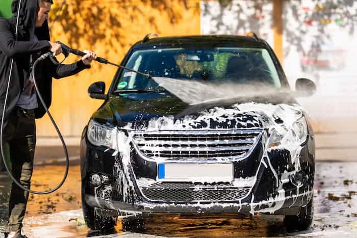 Person using a powerwash pressure washer to clean a black car