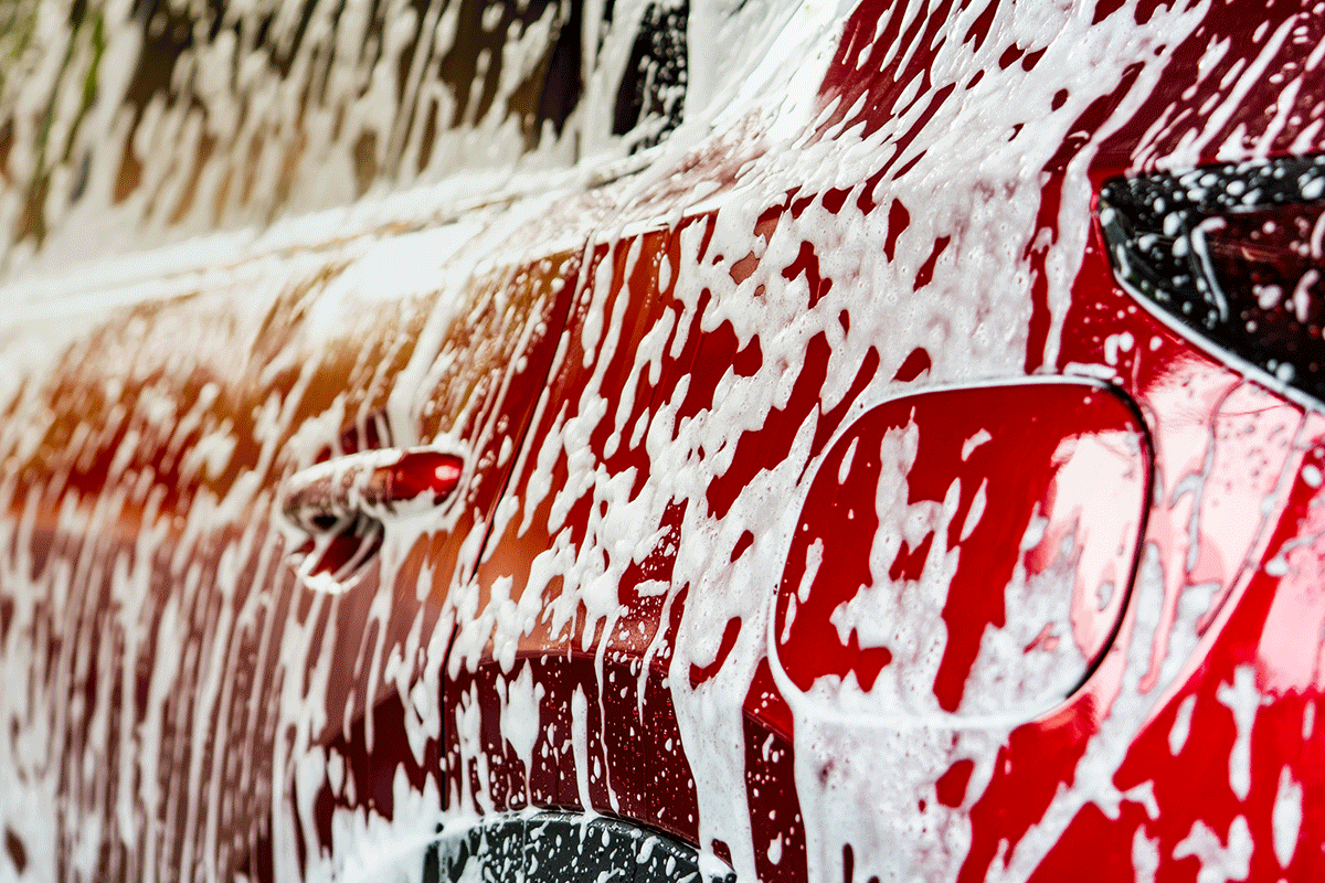 Red car covered in foam during a pre-wash process, highlighting innovative car cleaning techniques.