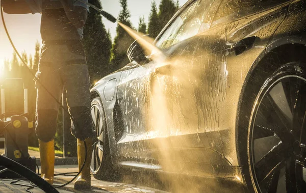 Professional using a high-pressure car wash machine to clean a car