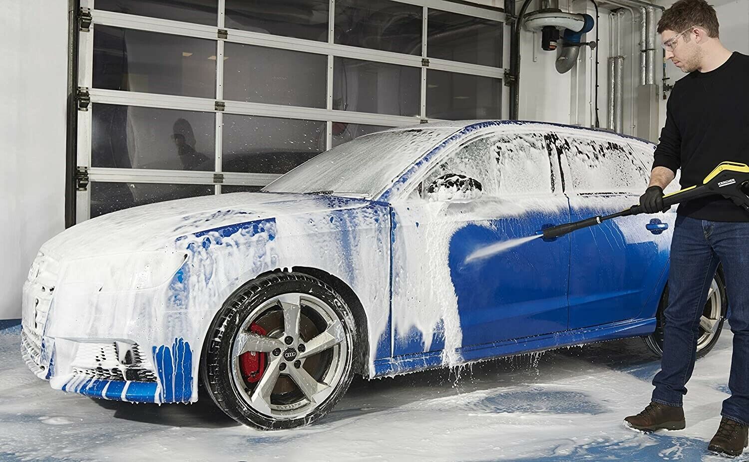 A professional hand car cleaner using a foam cannon to wash a blue car