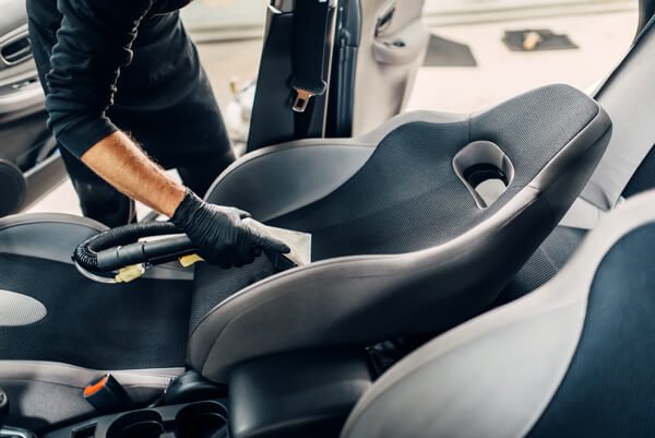 Professional cleaning car seats using specialised equipment during a hand car wash