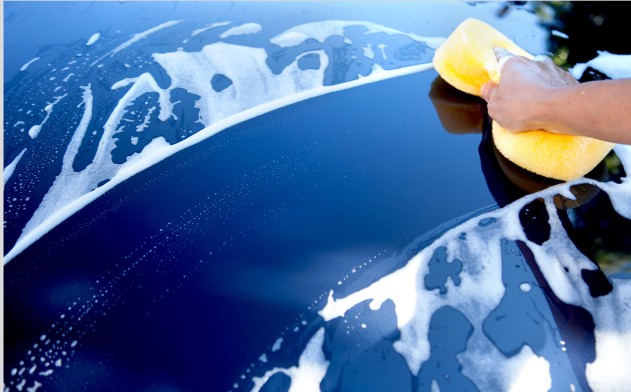 Hand washing a car with a sponge and soap suds for a quick 10-minute car wash in the UK.