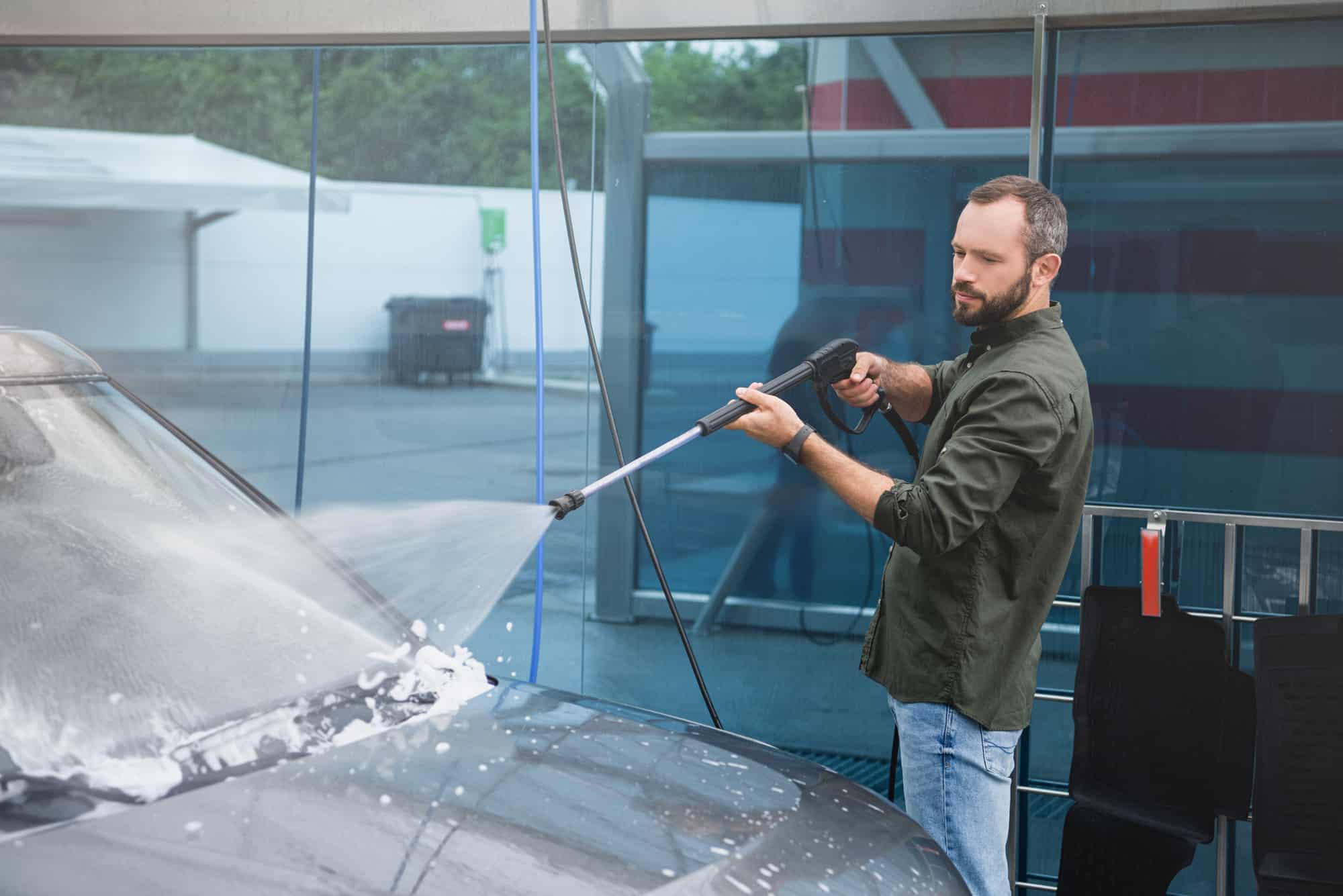 Man using a pressure washer at a self-service car wash, comparing to automatic car wash methods.